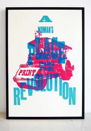 framed typographic poster that says a woman's place is in the revolution with a steamroller in the background.